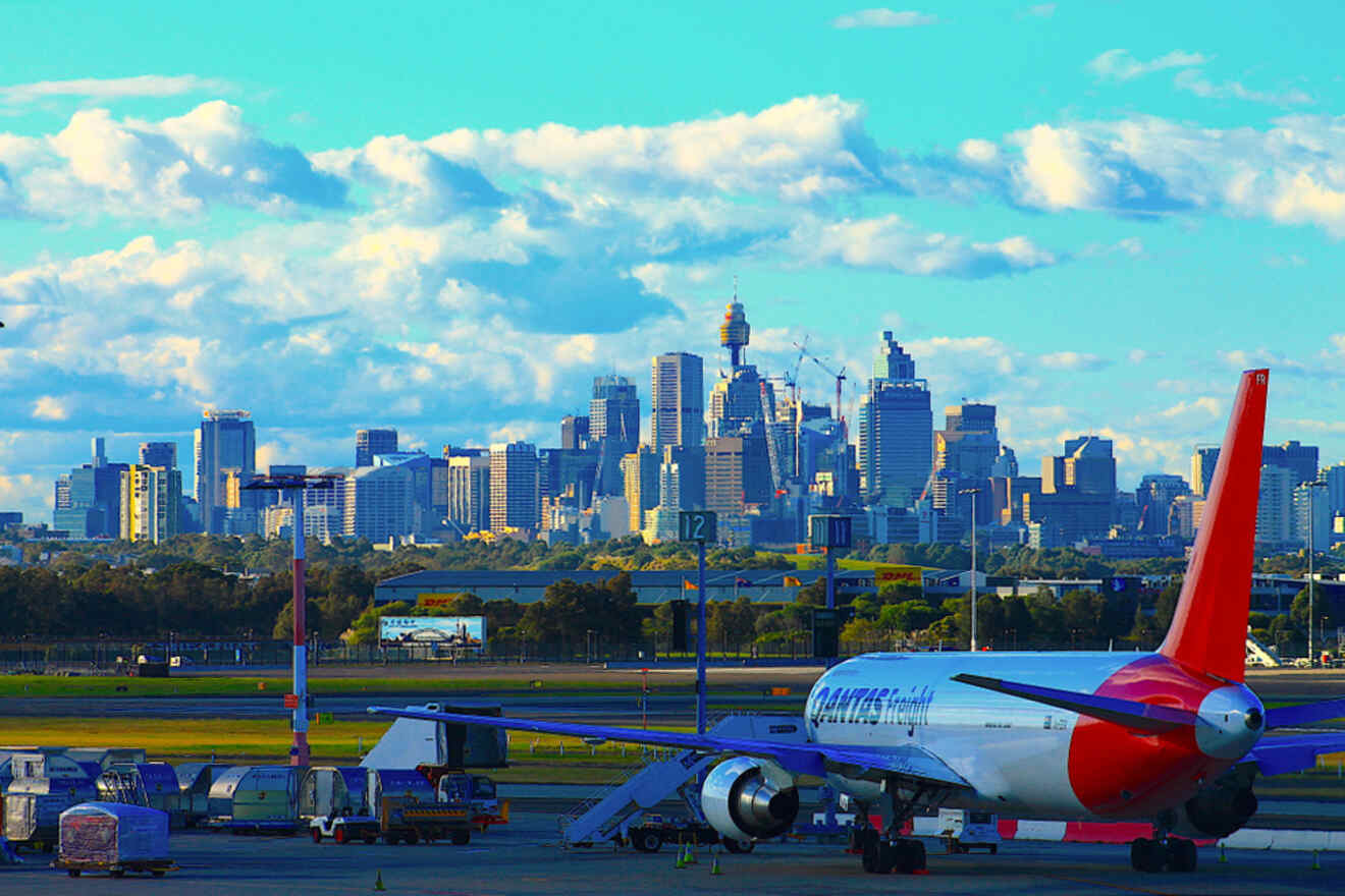 A commercial airplane is parked at an airport with the city skyline featuring tall buildings and a cloudy sky in the background.