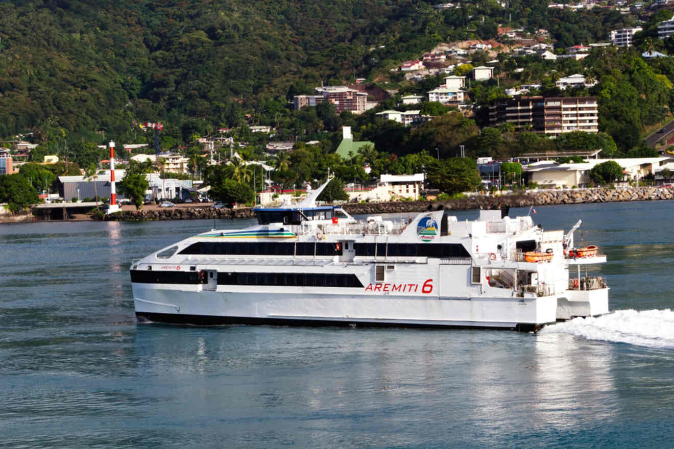 A French flag waving from a boat, with a distant view of the Aremiti Ferry 2 docked near a mountainous shore.