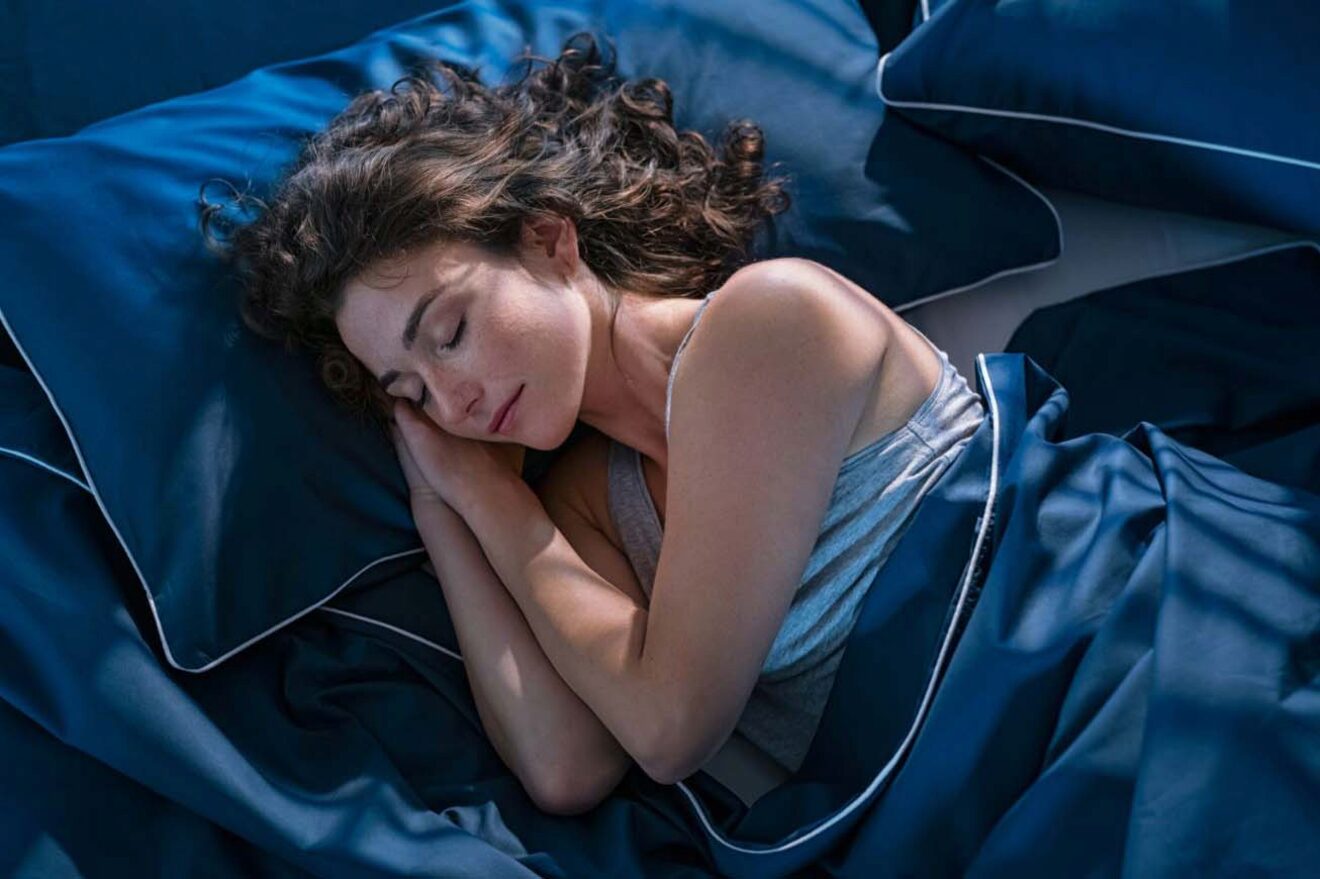 A woman peacefully sleeping in a bed with blue sheets.