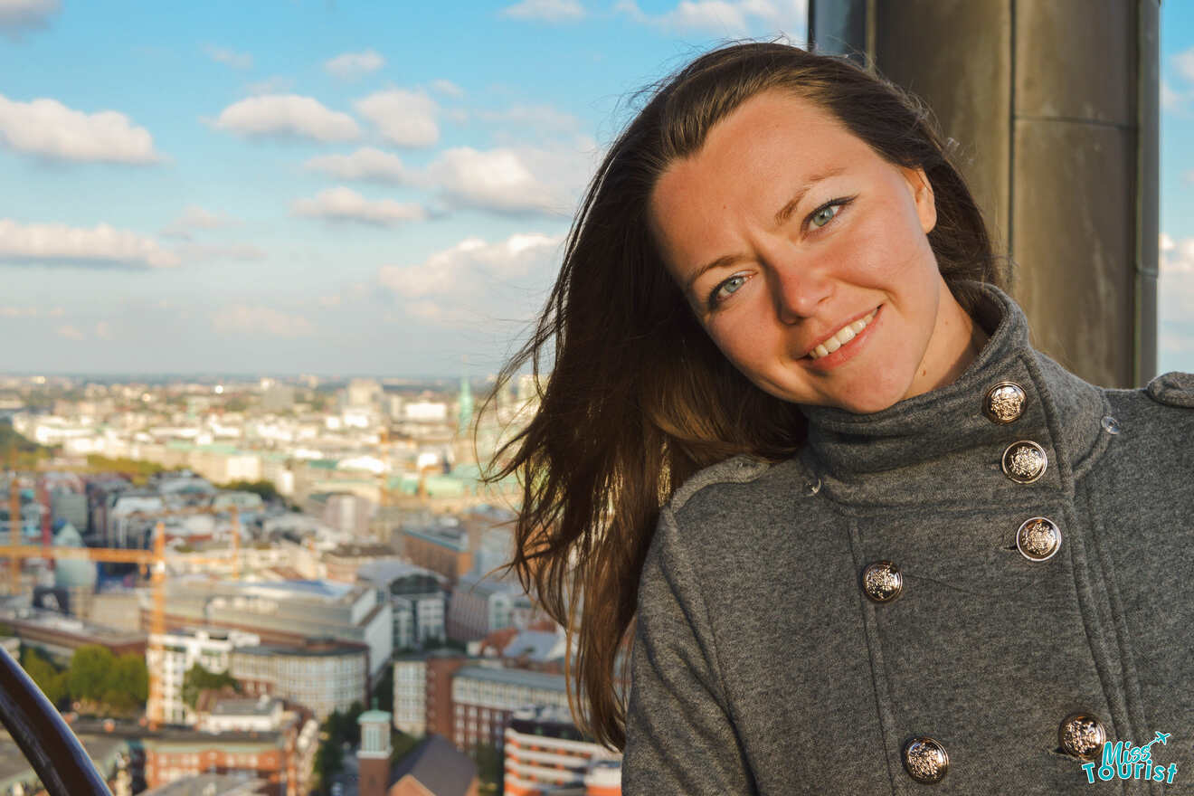 The founder of the page, Yulia, in a gray coat with metallic buttons stands outdoors, smiling at the camera with a cityscape in the background.