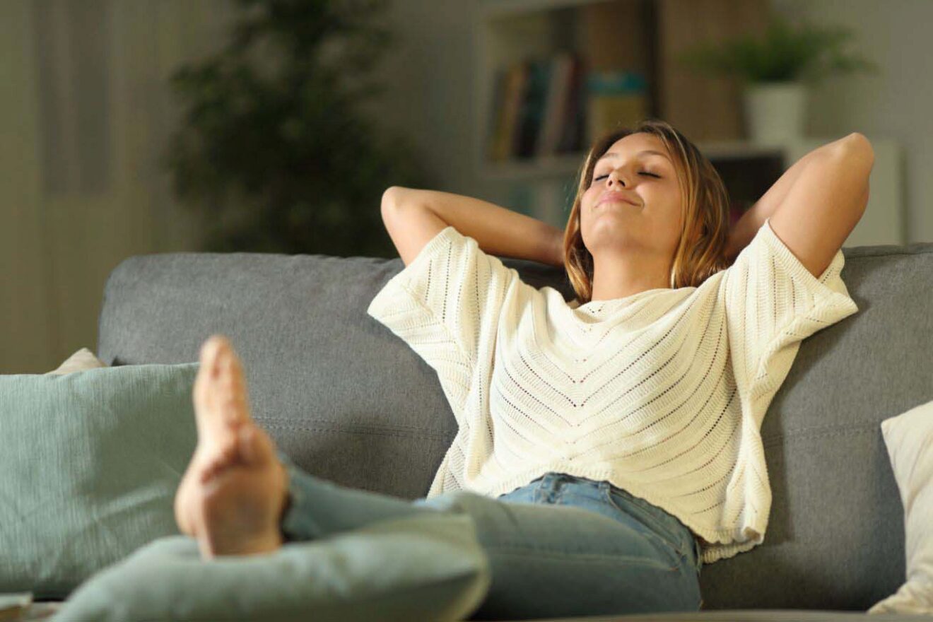 A woman relaxing on a couch with her hands behind her head.