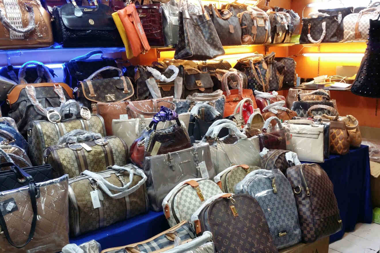 A market stall filled with various luxury handbags, showcasing brands like Gucci and Louis Vuitton, with bags arranged in rows and shelves.