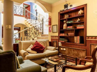 Cozy lounge with striped sofa, wooden bookshelf and wrought-iron staircase at Casa Aliso Hotel Boutique, Quito.