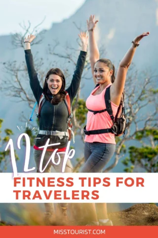 Two women wearing backpacks raise their arms in celebration on a hiking trail with mountains in the background. Text on image reads "12 Top Fitness Tips for Travelers. misstourist.com.