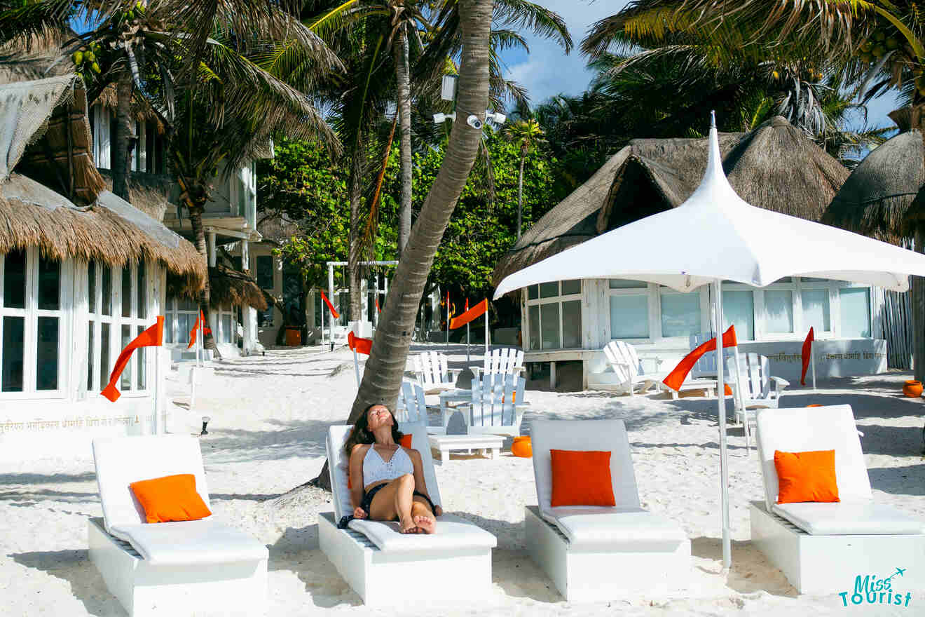 the author of the posts is reclining on a lounge chair at a beach resort with white sand, palm trees, and straw-roofed huts. Nearby, additional lounge chairs and umbrellas are visible with orange cushions.
