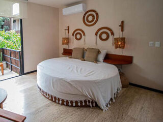A modern bedroom features a round bed with white bedding, two decorative wall lamps, three circular wall hangings, and an air conditioner above the bed.