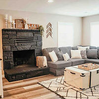 A cozy living room with a gray sectional sofa, a modern black fireplace, a white coffee table, and decorative accents on the walls.