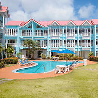 A brightly colored resort-style building with blue and white facades, surrounding a central outdoor swimming pool with lounge chairs and umbrellas.