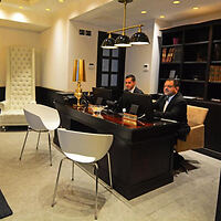 Hotel reception area with two well-dressed staff members seated behind a modern black desk, under elegant lighting.