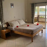 A cozy bedroom with a double bed adorned with red flower petals, located near a balcony overlooking lush greenery.