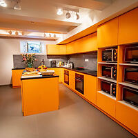 A modern kitchen with vibrant orange cabinets, an island, stainless steel appliances, and a small window above the countertop.