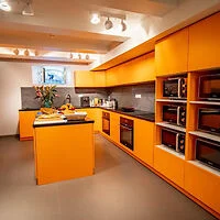 A modern kitchen with vibrant orange cabinets, an island, stainless steel appliances, and a small window above the countertop.