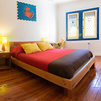 Cozy bedroom with a wooden bed, red and brown bedding, and colorful stained-glass windows.