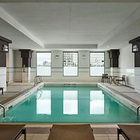 Indoor swimming pool with clear water, surrounded by lounge chairs and large windows offering a city view.