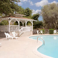 An outdoor pool surrounded by white deck chairs and a white wooden gazebo under a partly cloudy sky.