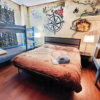 A bedroom with a double bed and a bunk bed, a pirate-themed mural on the wall, two bedside lamps, and a set of towels on the bed.