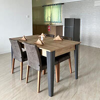 A minimalist dining area featuring a wooden table set with four chairs, napkins arranged in a triangle, and a small kitchenette in the background.