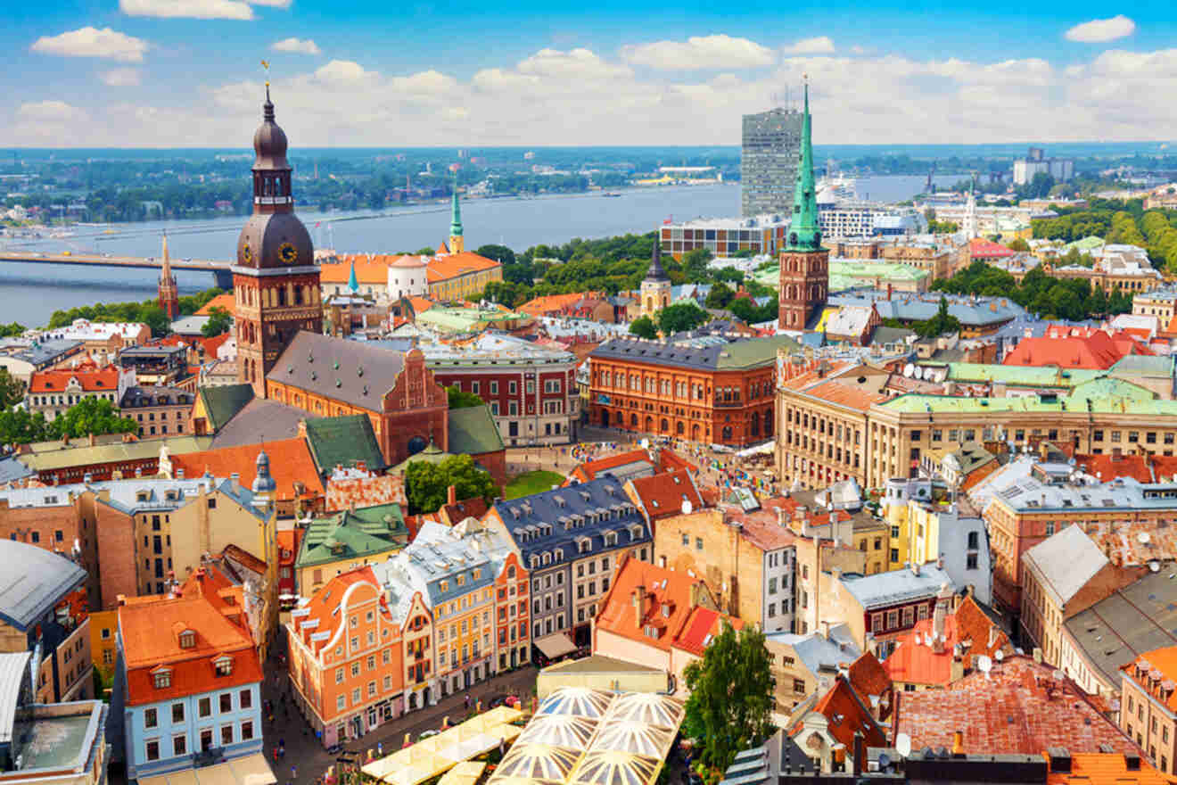 Aerial view of a city with colorful buildings, a large church with a clock tower, and a river in the background under a blue sky.