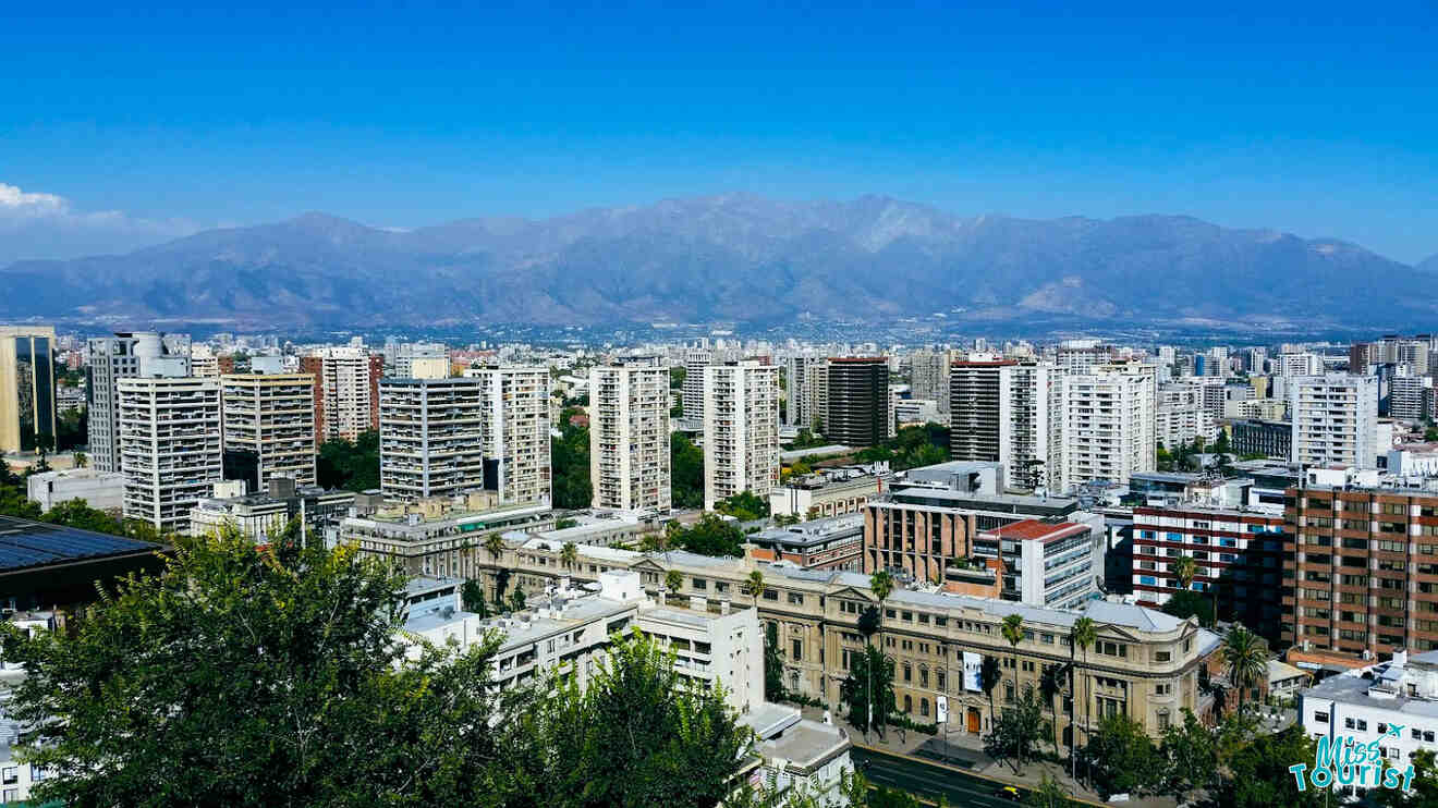 A panoramic view of Santiago de Chile with tall buildings against a backdrop of mountains under a clear blue sky.