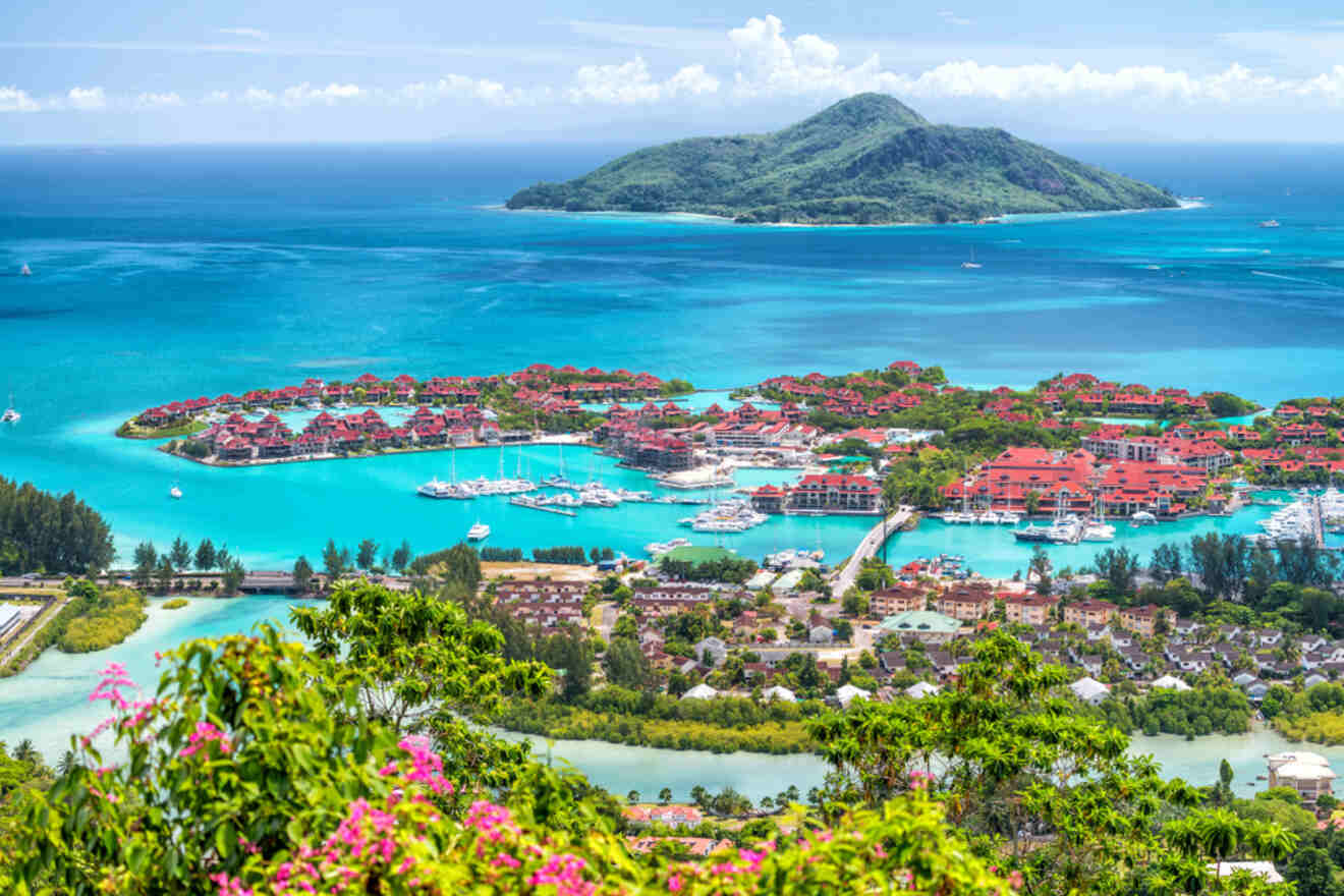 A stunning aerial view of a coastal resort with red-roofed villas surrounded by turquoise water, with a small island in the distance.