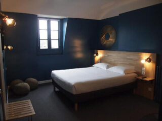 A dark blue bedroom features a bed with white linens, a wooden headboard with mounted reading lamps, a window allowing natural light, and wall decor above the headboard.