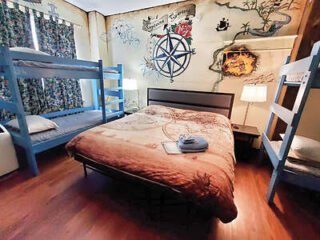 A bedroom with a double bed, two blue bunk beds, a nightstand with a lamp, and a wall painted with a pirate map mural.