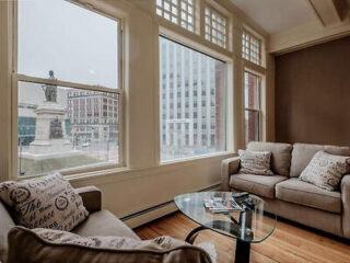 A living room with two gray sofas, a glass coffee table, and large windows offering a view of city buildings and a statue outside.