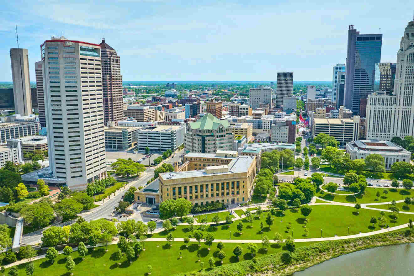 Aerial view of a cityscape featuring several tall buildings, including the prominent LeVeque Tower, surrounded by green parks and a river running alongside.