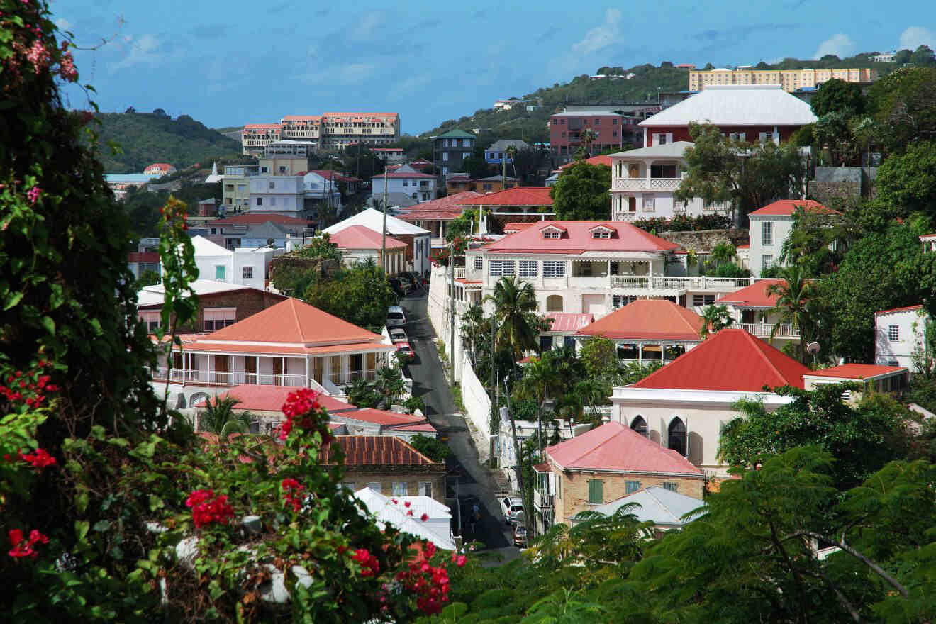 A scenic view of a town with red-roofed buildings and lush greenery on a hilly landscape under a clear blue sky.