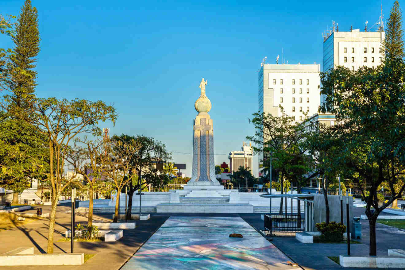 A monument featuring a globe-topped spire stands centrally in a public plaza, flanked by trees and surrounded by tall buildings.