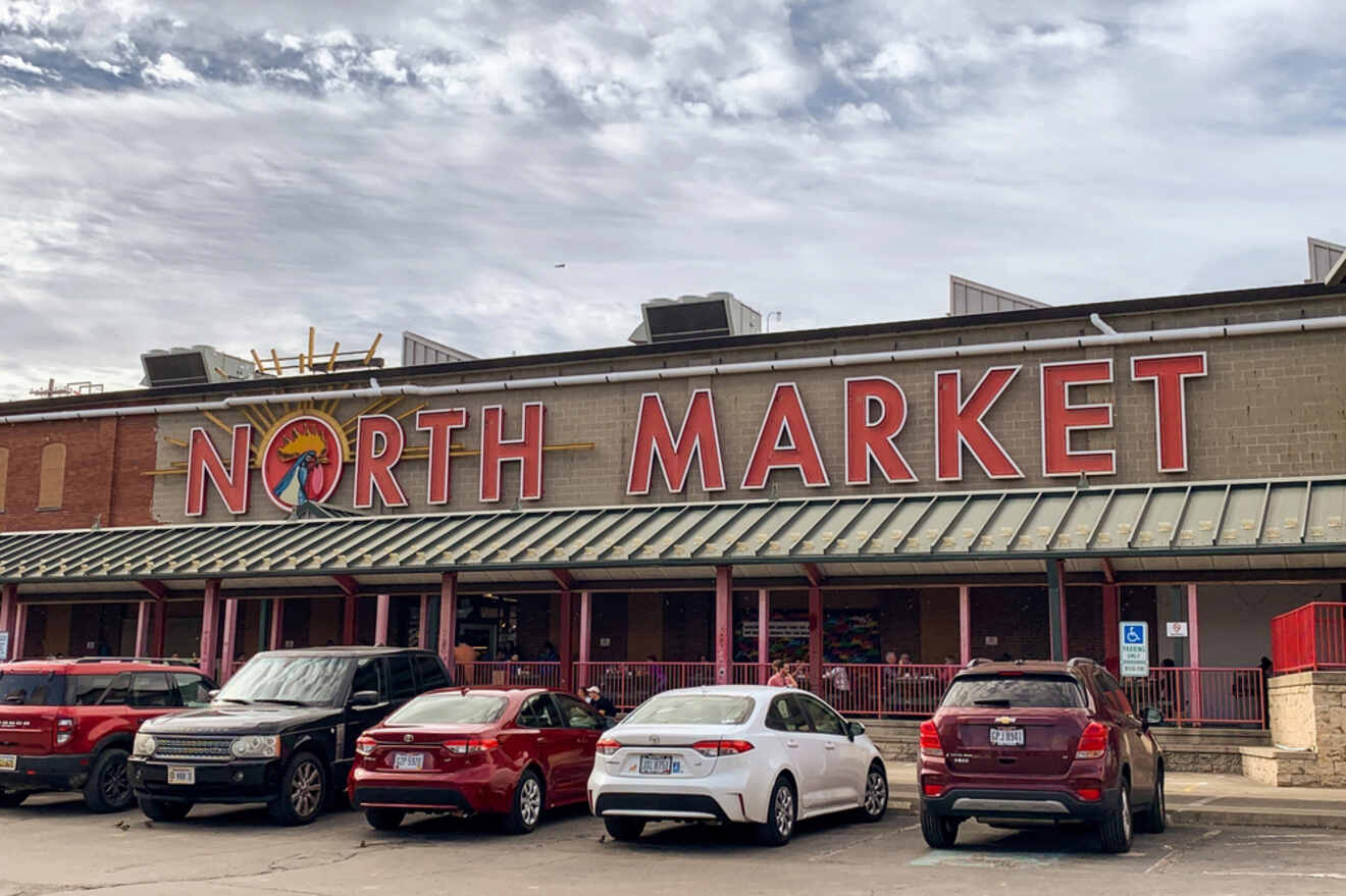 Exterior view of the North Market building with a parking lot in front, featuring several parked cars under a partly cloudy sky.