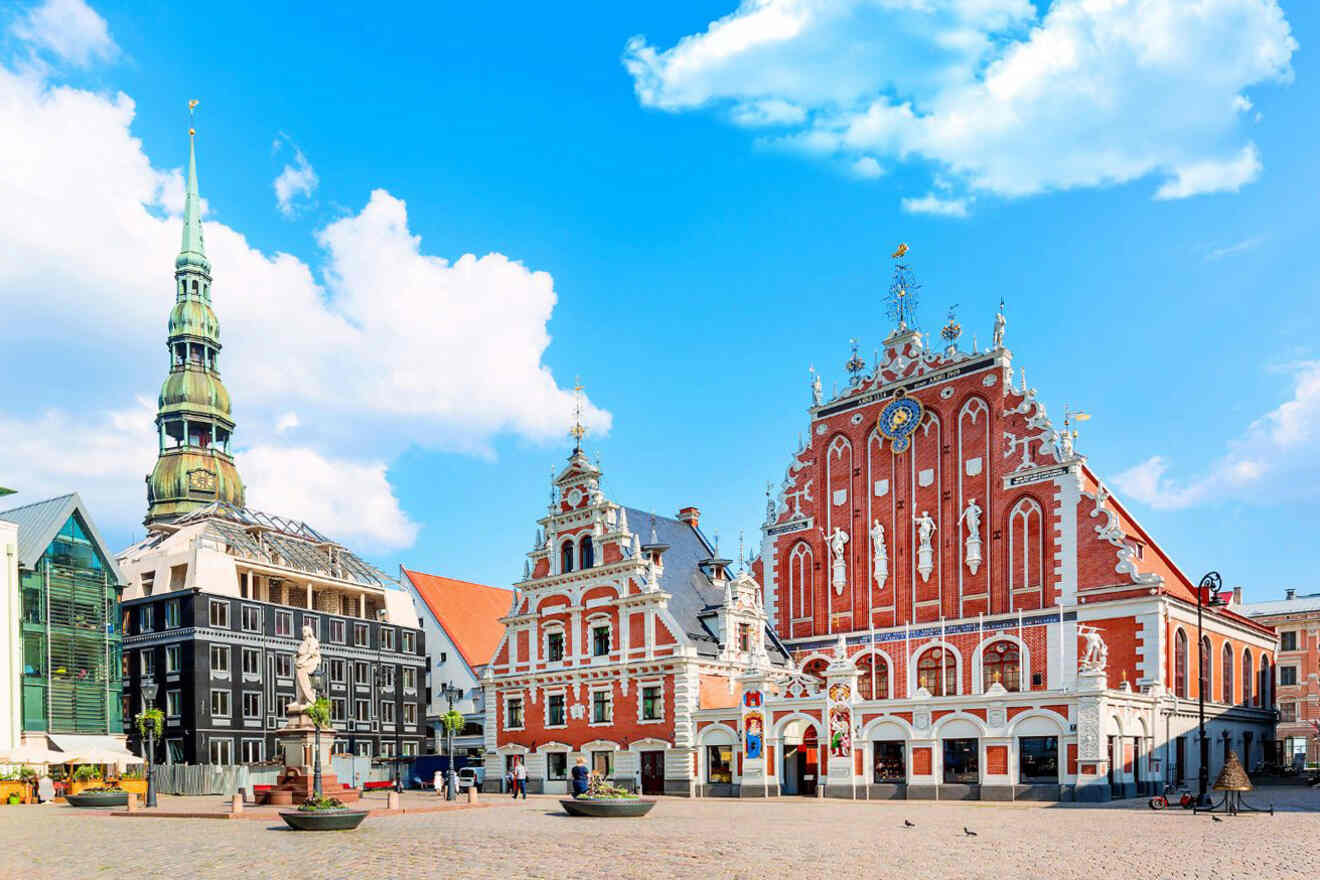 A historical European square with ornate buildings, including House of the Blackheads, and a tall church tower under a blue sky with scattered clouds.