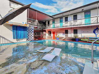 A small pool in a courtyard surrounded by a two-story building, with lounge chairs partially submerged in shallow water and a colorful mural on the wall.