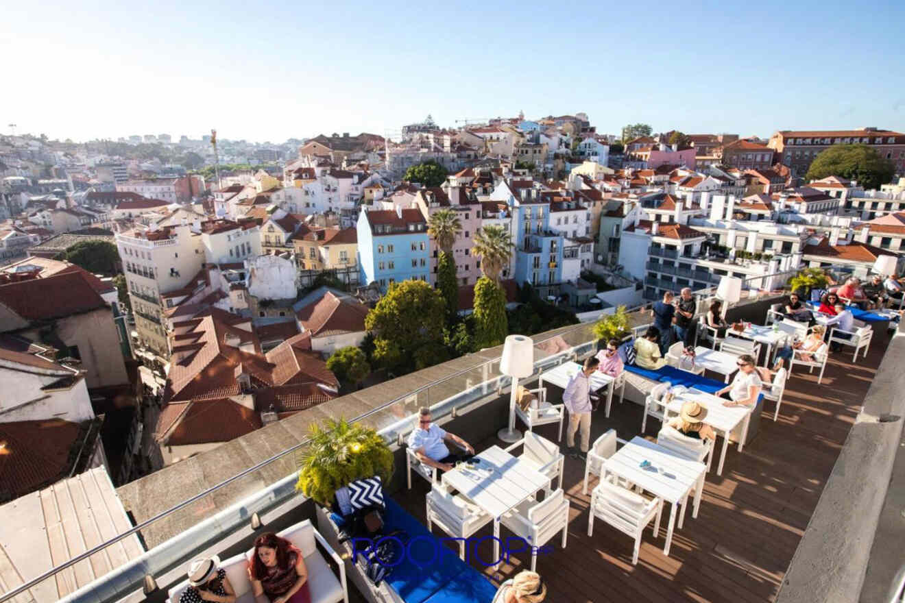 Outdoor restaurant on a rooftop, with people dining at tables, overlooking a cityscape with traditional-style buildings and scenic views.