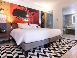 Modern hotel room featuring a large bed with bold artwork on the wall and an ensuite bathroom.