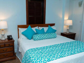 A cozy bedroom with a wooden bed frame, white bedding with turquoise pillows, and matching decor, flanked by nightstands with lamps.