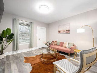 Cozy living room with a pink sofa, modern armchair, circular glass coffee table, green curtains, floor lamp, large plant, wall art, and a cowhide rug on a polished wood floor.