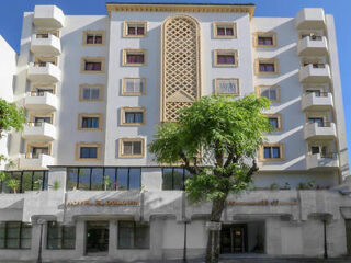 A large hotel building with a cream-colored facade and intricate architectural details, surrounded by greenery.