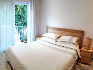 A simple, well-lit bedroom with a wooden bed frame and a view of a green balcony.