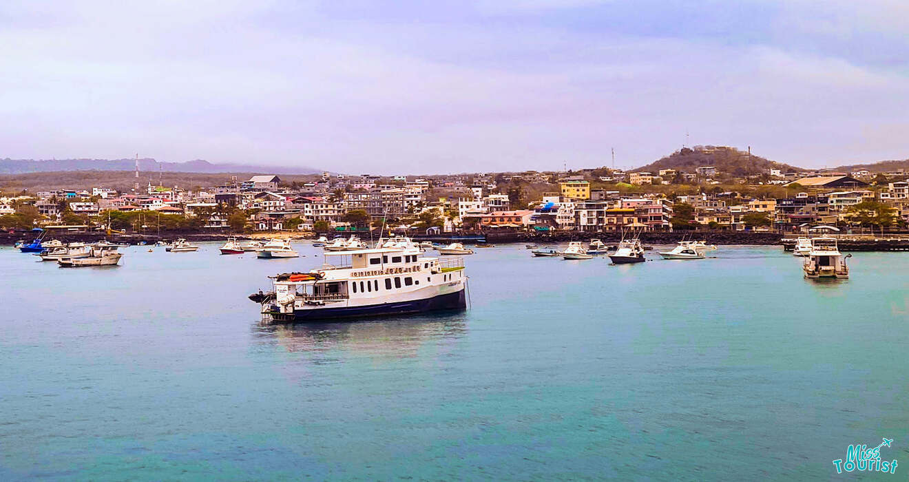 A coastal town with numerous buildings, boats, and yachts docked in a calm harbor under a partly cloudy sky.