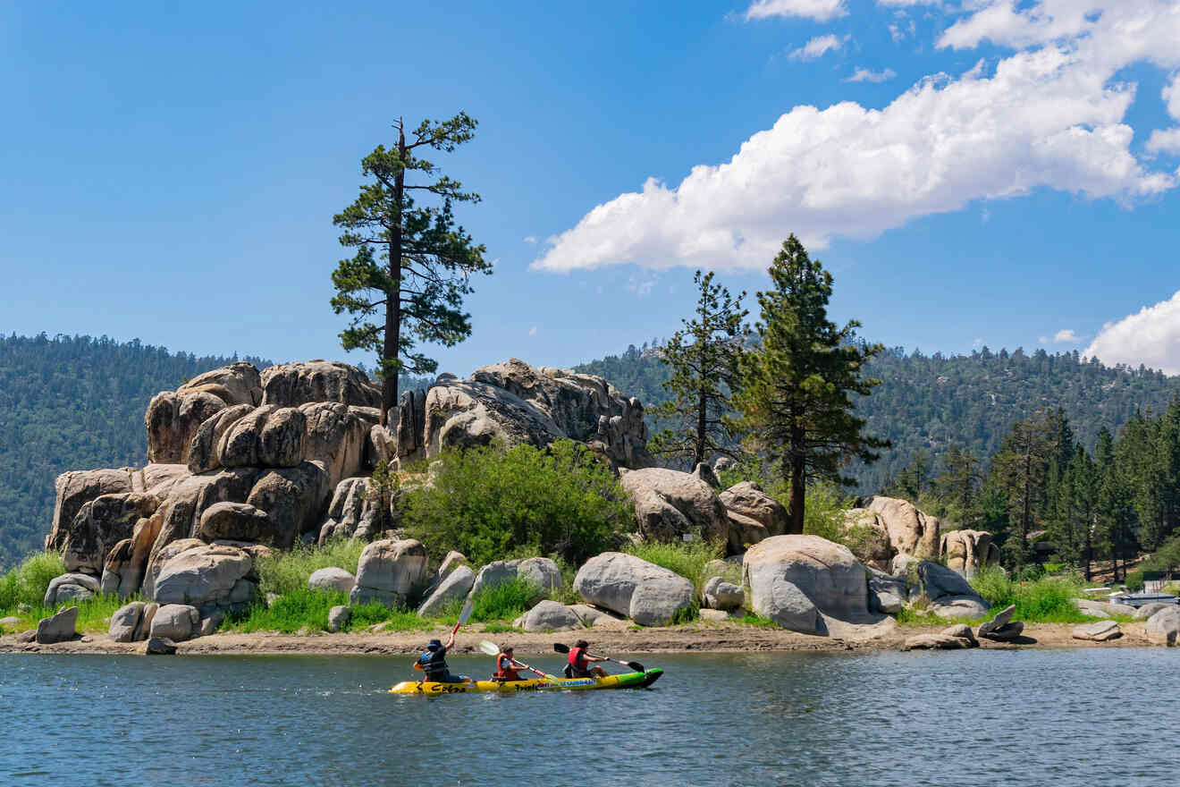 Three people are kayaking on a calm lake near a small rocky island with trees, under a clear blue sky.