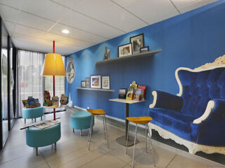 A modern waiting area with a blue theme featuring a blue armchair, small tables with chairs, bookshelves, framed photos, and informational brochures on display.