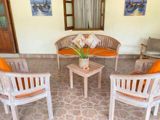 An outdoor seating area with wooden chairs and a table, all with orange cushions, set on a tiled patio with wall art in the background.