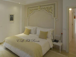 An elegant bedroom with a white bed, decorative headboard, and minimalistic design