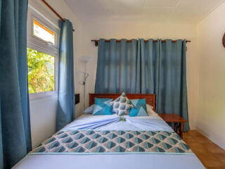 A small, cozy bedroom with a double bed dressed in patterned bedding, with teal curtains and a wooden nightstand.