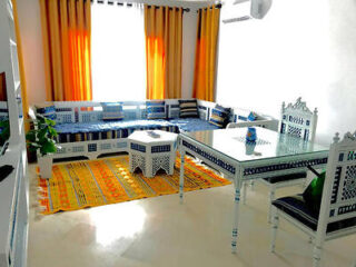 A bright living room with traditional Tunisian furniture, colorful curtains, and a patterned rug.