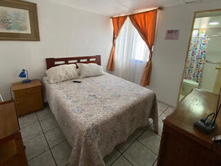 Simple bedroom with a double bed covered in a floral quilt, next to a window with orange curtains.