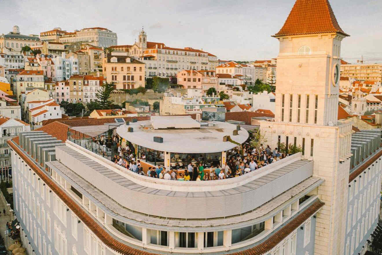 A rooftop gathering is taking place on a large building in a densely built area with historic architecture, featuring red-tiled roofs and white buildings under a clear sky.