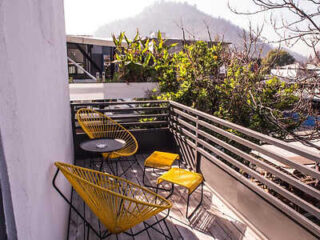 Cozy balcony with yellow chairs and a view of lush greenery and distant hills.