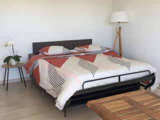 A neatly made bed with a geometric-patterned duvet cover, beside a small round table with a potted orchid and a tall tripod floor lamp in a minimalist bedroom.